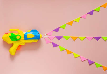 Water gun spray out with colorful party flag for Songkran festival celebration on pink color background. Minimal holiday concept.の写真素材