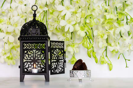 Candle with flame in lantern and dates fruit with orchid flower on white background for the Muslim feast of the holy month of Ramadan Kareem.の写真素材