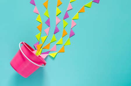 Pink bucket splash out with colorful party flag that set as water for Songkran festival celebration on blue background. Minimal holiday concept.の写真素材