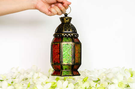 Hand holding lantern on white background with white orchid flower for the Muslim feast of the holy month of Ramadan Kareem.の写真素材