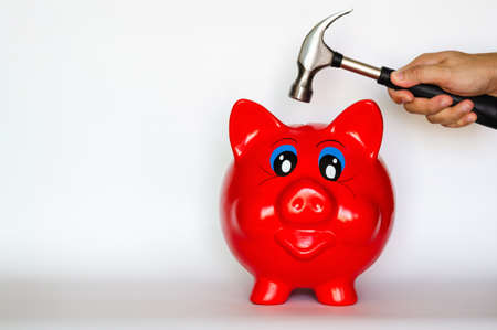 Red piggy bank with hand holding the hammer puts on white background with space for text.の写真素材
