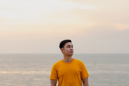 Asian man smiling and looking up with sea and sky background. Good mental health concept.の写真素材