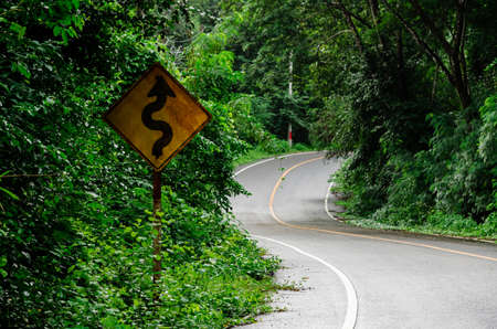 Old traffic sign placed beside along the messy road from tree and grass.の写真素材