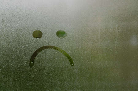 Face expession as boring and sad painted on window which fogged up after rain with blurred green color background.の写真素材