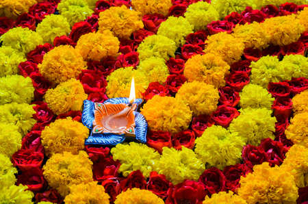 Decorative marigold and rose flowers rangoli for Diwali festival with clay diya lamp lit with flame.の写真素材