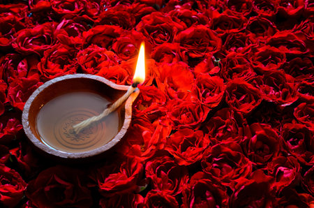 Decorative red rose flower rangoli for Diwali festival with clay diya lamp lit with flame.