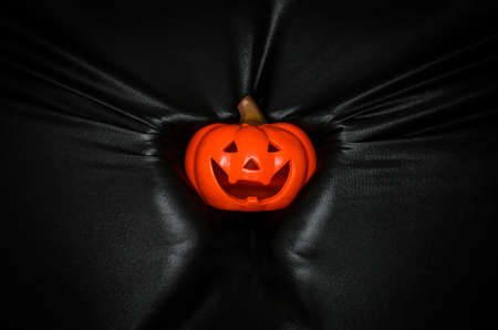 Halloween pumpkin holding by hand pressing through black fabric background. Halloween festival concept.の写真素材