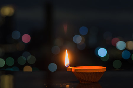 Selective focus on the flame of clay diya lamp with colorful city bokeh lights. Diwali festival concept.の写真素材