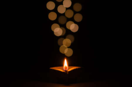 Selective focus on flame of clay diya lamp lit on dark background with bokeh lights. Diwali festival...