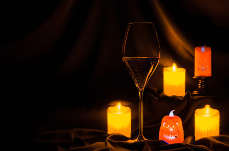 A glass of white wine with small halloween lantern and blurred focus candle on dark cloth background. Halloween dinner party concept.の写真素材