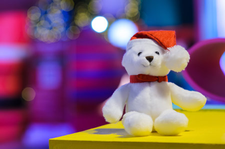 Selective focus on Santa claus teddy bear eyes who wearing hat sitting in front of colorful blurred background and bokeh lights.の写真素材