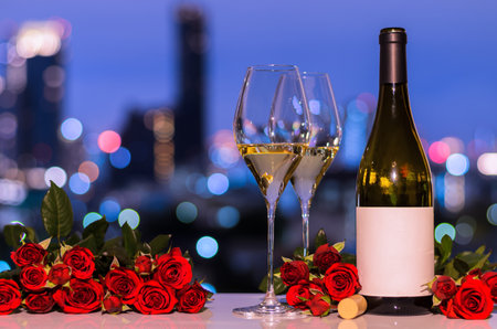 Selective on first glass of white wine with blurred bottle and red roses on colorful bokeh light from city background for Valentines dining concept.の写真素材