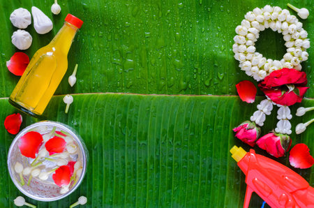 Thailand songkran festival background with water gun, garland, scented water and flower in silver bowl put on wet banana leaf.の写真素材