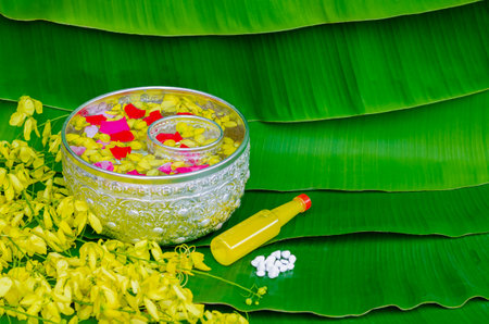 Songkran festival background with flowers in water bowls, scented water and marly limestone for blessing on wet banana leaf background.の写真素材