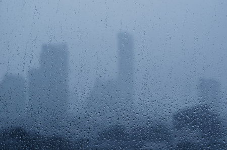 Rain drop on glass window in monsoon season with blurred city buildings background.の写真素材
