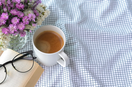 A cup of coffee with book and spectacles on bed in morning. Stay home and relaxing concept.