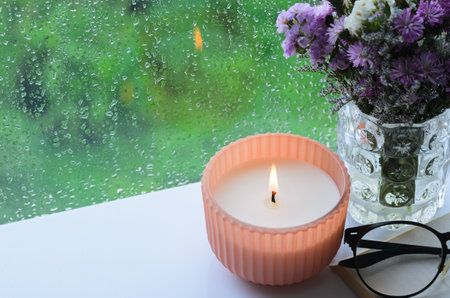 Flame burning at aroma candle puts near by window with rain drop in monsoon season. Zen and relax concept.の写真素材