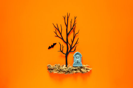 Halloween background with tombstone on dried grass and black tree with a bat on orange background. Minimal concept.の写真素材