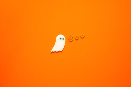 Halloween background with gel stickers of white ghost sheet and alphabets on orange background. Minimal concept.の写真素材