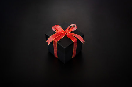 Black gift box with red ribbon tie with the bow puts on black background for Black Friday shopping day concept.の写真素材