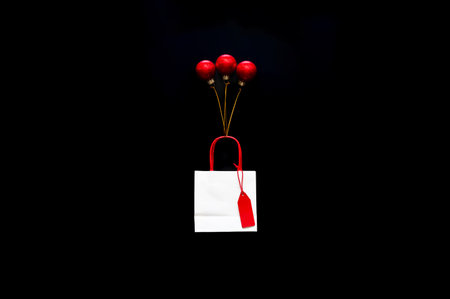 White shopping bag and red price tag with balloon that made from christmas ornaments on black background for Black Friday shopping day concept.の写真素材