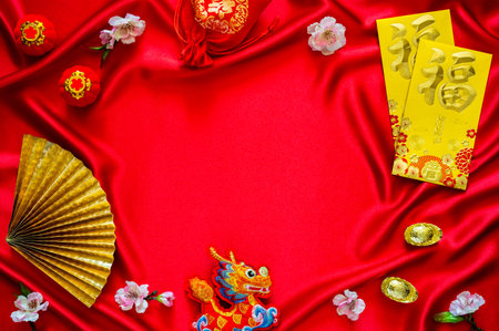 Chinese new year background with envelope packets or ang bao (word mean blessing), red bag and ingots (words mean wealth), hanging pendant dragon on red colth background.の写真素材