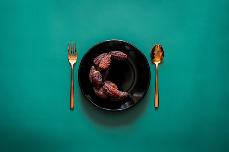 Date fruits set as moon symbol on black plate with golden fork and spoon on green background for the Muslim feast of the holy month of Ramadan Kareem.の写真素材