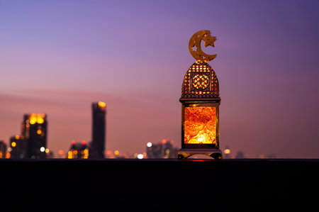 Golden lantern that have moon symbol on top with dusk sky and city background for the Muslim feast of the holy month of Ramadan Kareem.の写真素材
