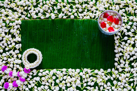 Flowers in water bowl for blessing with garland on empty space of wet banana leaf and jasmine...