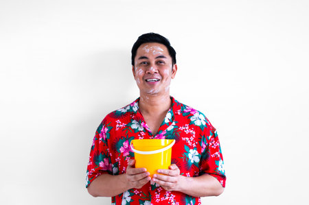 Thai male with white clay filler on face wearing colorful shirt holding bucket for Songkran or Water festival in Thailand concept.の写真素材