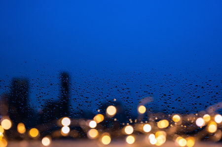 Raindrops on glass window with golden lights and blurred city background.の写真素材