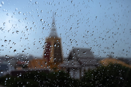 Rain drops on glass window in monsoon season with blurred temple building background.の写真素材