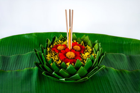 Krathong that have 3 incense sticks and candle decorates with red and yellow flowers puts on banana leaf for Loy Krathong festival on white background.の写真素材