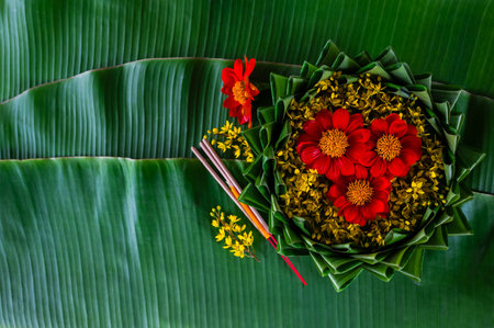 Krathong decorates with red and yellow flowers that have blurred focus of 3 incense sticks and candle put on banana leaf for Loy Krathong festival.の写真素材