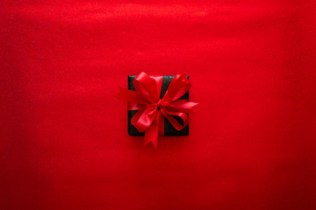 Black Friday concept with single luxurious black gift with red ribbon on vibrant red glitter background.の写真素材