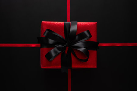 Black Friday with a stunning red gift box with a black satin bow is centered on crossing red ribbons on a dark black background.の写真素材