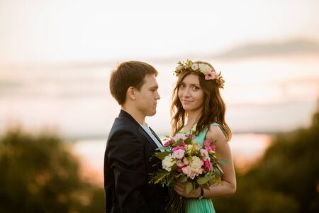 A Young couple in love outdoor at the sunset - girl in a wreath looks into the camera