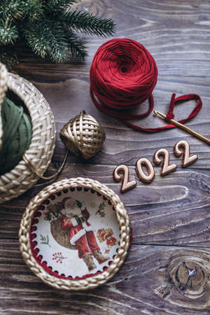 Christmas and New Year 2022 greeting card, balls of knitted yarn, crochet hook and knitted basket on a wooden table, top viewの写真素材