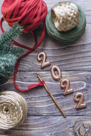 Christmas and New Year 2022 greeting card, balls of knitted yarn, crochet hook and knitted basket on a wooden table, top viewの写真素材