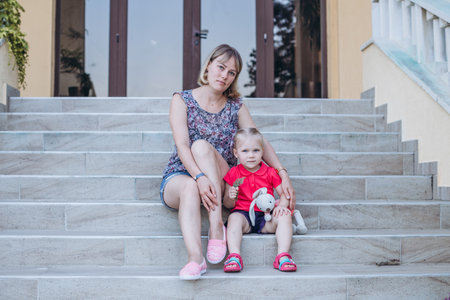 mother and daughter sitting on the steps of the house and holding a toyの写真素材