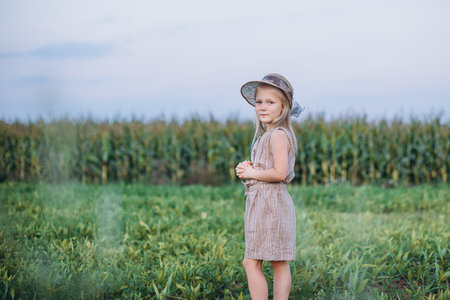 a girl in a beautiful hat admires the view of a corn fieldの写真素材