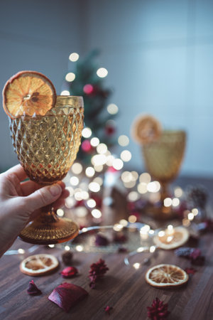 Hand holding golden wine glass with dried orange slices and Christmas decoration on backgroundの写真素材