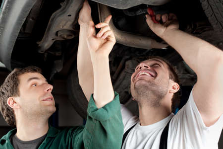 Two mechanics repairing car in garage under the car.の写真素材