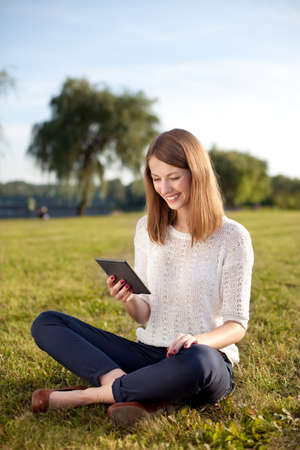 Young woman reading e-book outdoor sitting on grass
