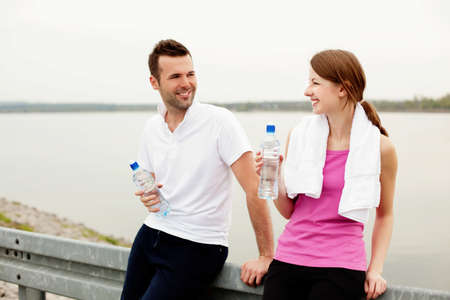 Happy woman and man talking and drinking water after exercise