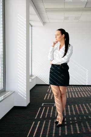 Photo of a female executive standing by a window and thinkingの写真素材