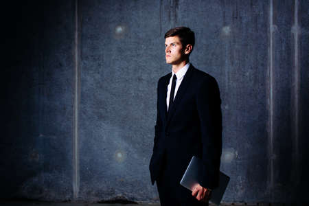 Photo of a standing elegant businessman holding a laptopの写真素材
