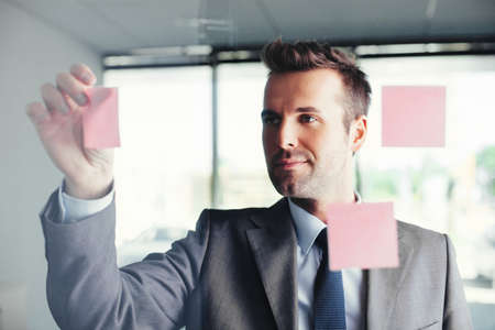 Young businessman sticking notes on a glass wallの写真素材