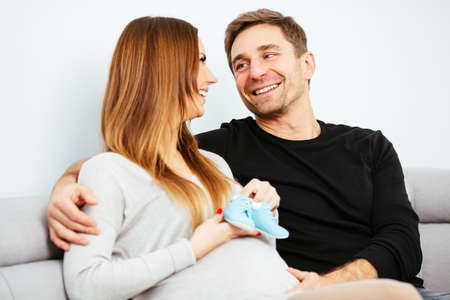 Happy pregnant couple sitting on a sofa and hugging