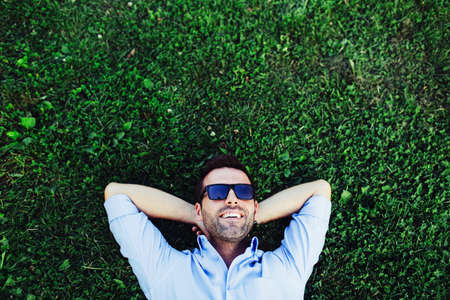 Portrait of a young happy man relaxing on the grass with his hands under the headの写真素材
